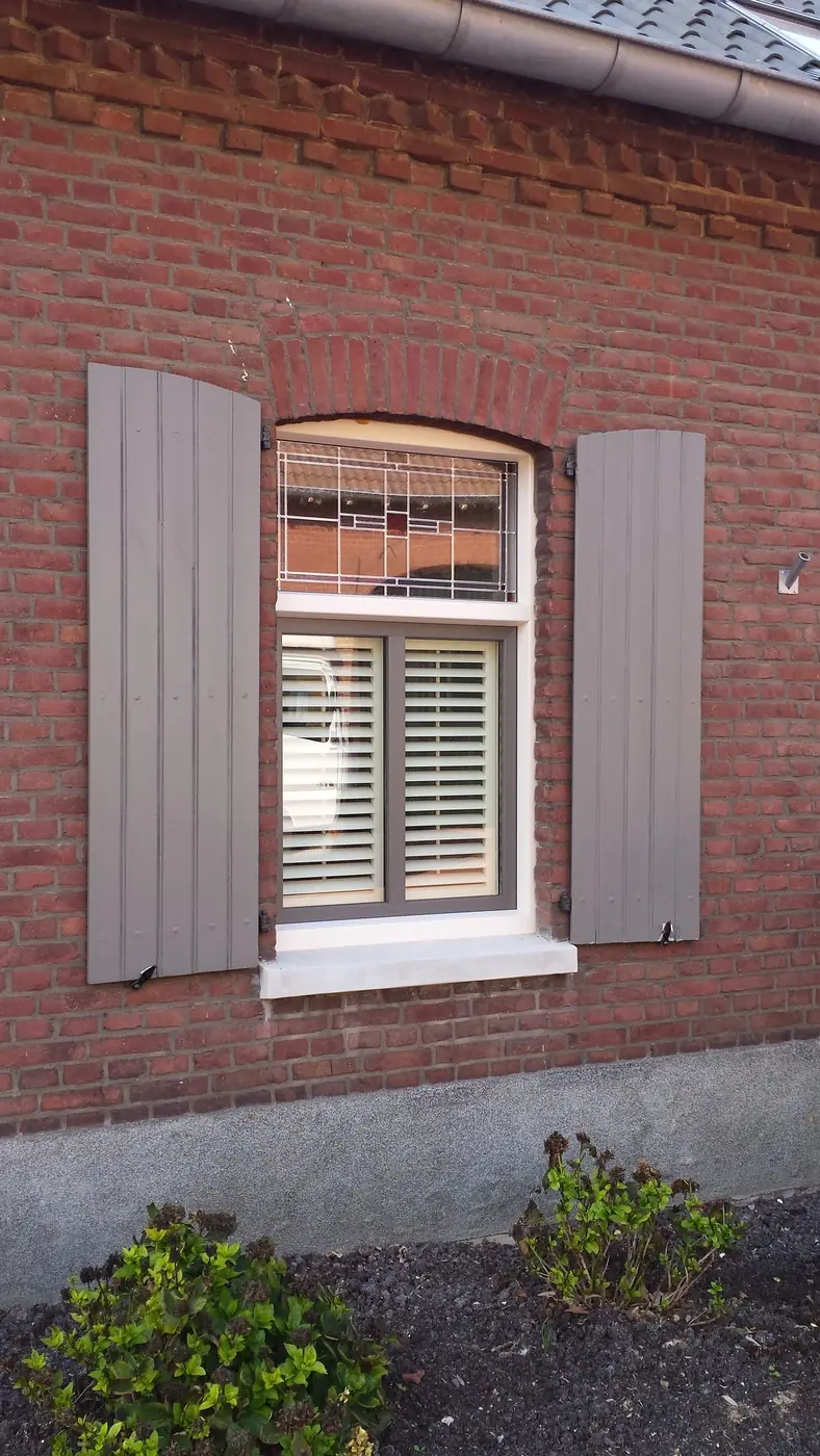 Shutters achter een boogvenster in een bakstenen gevel, met luiken ernaast